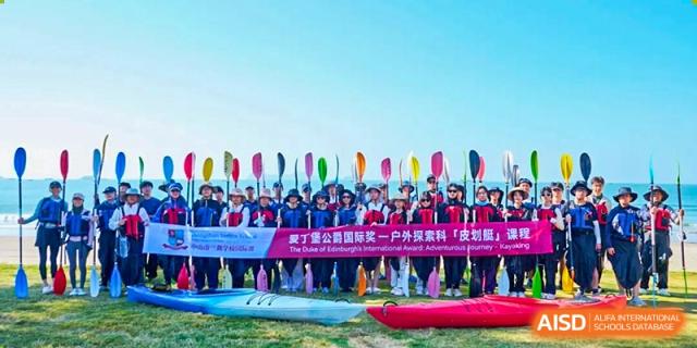 A group of students in life jackets stands on a beach holding upright paddles behind their colorful kayaks for a commemorative photo at Zhongshan Sanxin School International Department.