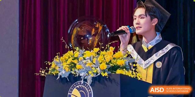 A graduate in formal academic regalia speaks into a microphone at a podium decorated with vibrant yellow flowers during a commencement ceremony at Beijing Chaoyang KaiWen Academy.