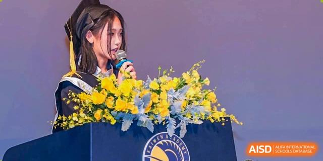 A female graduate delivers an emotional farewell speech from a flower-adorned lectern during the formal graduation day celebrations held on campus at Beijing Chaoyang KaiWen Academy.