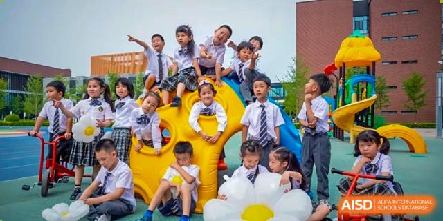 A group of elementary students in matching school uniforms poses together while playing on a colorful yellow and blue outdoor jungle gym at Beijing Chaoyang KaiWen Academy.