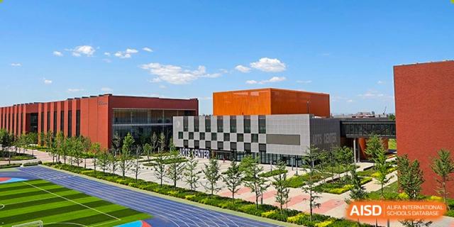An aerial perspective highlights the expansive school grounds including the blue athletic track and modern grey and orange academic buildings at Beijing Chaoyang KaiWen Academy.