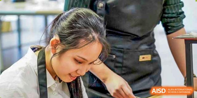 A focused female student works on a detailed project during a hands-on vocational or arts workshop inside a well-lit and modern classroom at Beijing Chaoyang KaiWen Academy.