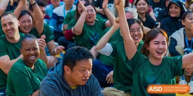 Enthusiastic parents and teachers cheer and raise their hands during a high-energy school spirit event held in a packed indoor gymnasium at Beijing Chaoyang KaiWen Academy.