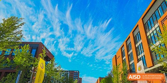A beautiful view of the modern school campus architecture is framed by a vibrant blue sky with unique wispy cloud formations at Beijing Chaoyang KaiWen Academy.