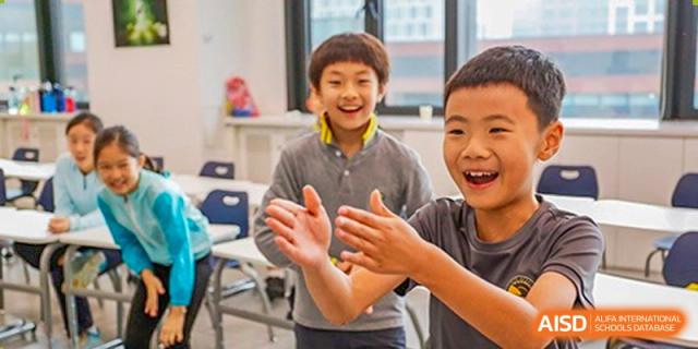 Two joyful elementary students clap and laugh together during an interactive and fun classroom activity designed to foster teamwork at Beijing Chaoyang KaiWen Academy.