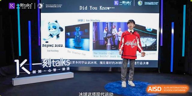 A student in a red jersey stands on a circular stage to deliver a talk about ice hockey as part of a "K-talks" presentation at Beijing Chaoyang KaiWen Academy.