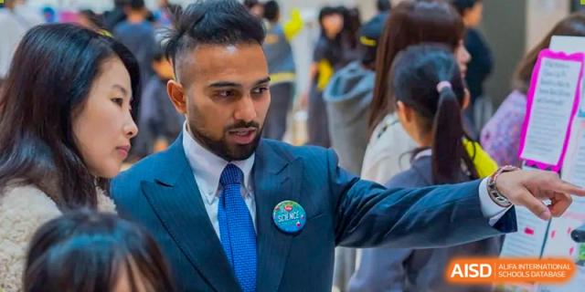 A male faculty member in a professional blue suit engages in an earnest conversation with a student during a campus networking event at Beijing Chaoyang KaiWen Academy.