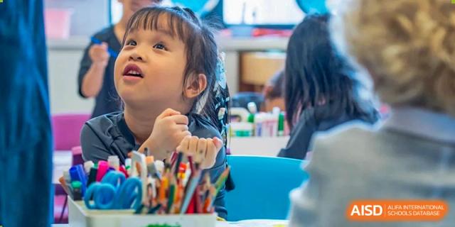 A young girl with a curious expression looks upward while surrounded by colorful school supplies in a bright and inviting classroom at Beijing Chaoyang KaiWen Academy.