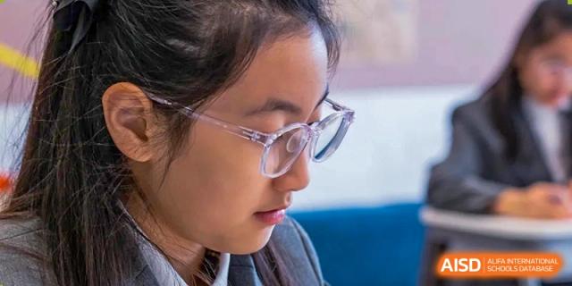 A close-up profile shot shows a focused student with glasses working intently on a project in a quiet and studious environment at Beijing Chaoyang KaiWen Academy.