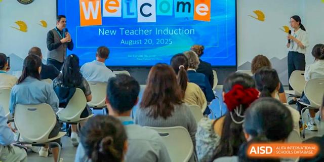 Educators sit in a lecture hall and watch a large digital screen during a formal "New Teacher Induction" ceremony held on campus in August at Beijing Chaoyang KaiWen Academy.