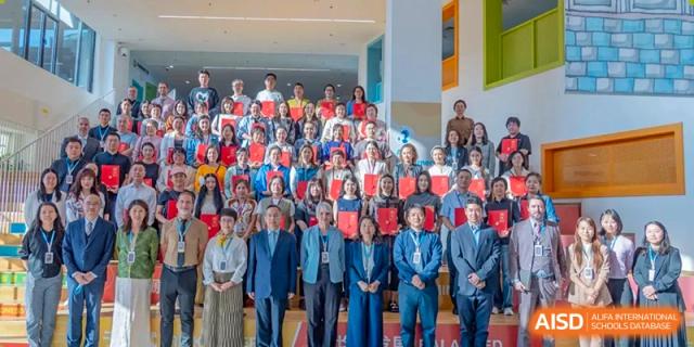 A large group of faculty members and administrators in professional attire poses for a formal commemorative photo on a tiered stage during an assembly at Beijing Chaoyang KaiWen Academy.