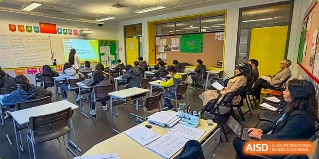 Students sit at their desks in a modern classroom while an instructor leads a lesson using a digital whiteboard and integrated technology at Beijing Chaoyang KaiWen Academy.