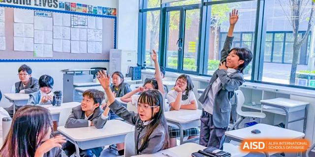 Several elementary students raise their hands enthusiastically to answer a question during an engaging and interactive lesson in a bright classroom at Beijing Chaoyang KaiWen Academy.