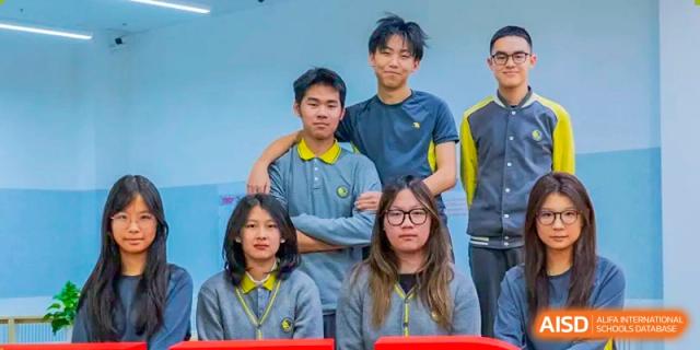 A group of secondary students in grey and yellow school uniforms poses for a friendly portrait in front of a blue background on the campus of Beijing Chaoyang KaiWen Academy.