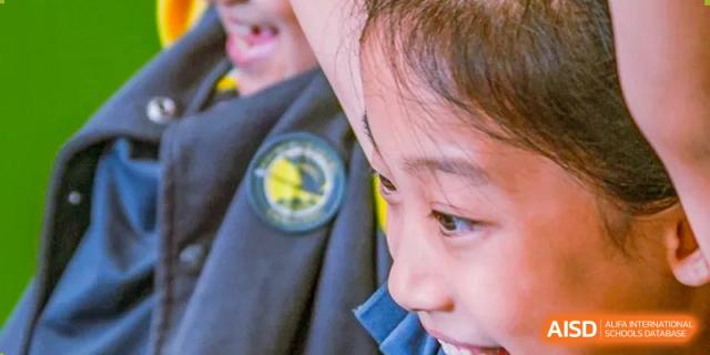 A close-up shot captures the side profile of a focused student wearing a school uniform jacket featuring the official gold and blue crest at Beijing Chaoyang KaiWen Academy.