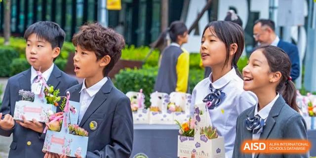 Two young students in formal uniforms stand outdoors next to a table of flowers while participating in a special campus celebration at Beijing Chaoyang KaiWen Academy.