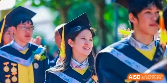 A female graduate in a black academic gown and cap with a yellow tassel smiles warmly while looking toward the side during her formal commencement ceremony at Beijing Chaoyang KaiWen Academy.