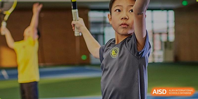 A young student focuses intensely while preparing to swing a golf club during an outdoor physical education lesson on the green campus at Beijing Chaoyang KaiWen Academy.