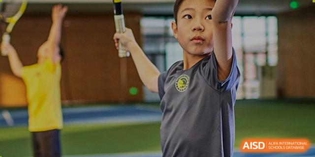 A young student focuses intensely while preparing to swing a golf club during an outdoor physical education lesson on the green campus at Beijing Chaoyang KaiWen Academy.