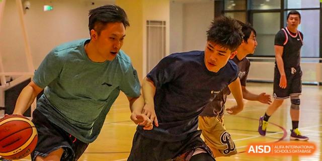 Two male students compete for the ball during a fast-paced and high-energy indoor basketball game held in the professional school gymnasium at Beijing Chaoyang KaiWen Academy.