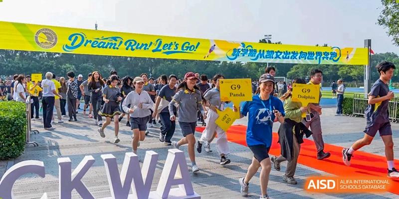 Excited students in sports gear race past a "Dream, Run, Let's Go" banner during a track and field competition held on the school grounds at Beijing Chaoyang KaiWen Academy.