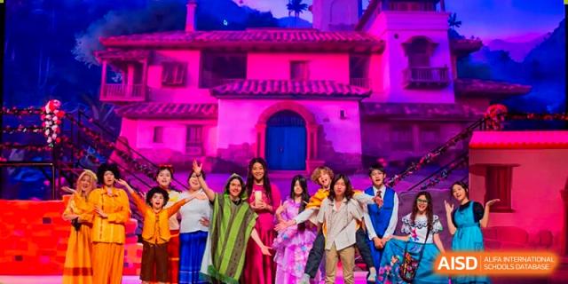 A cast of students in vibrant and diverse costumes performs a theatrical musical production on a stage with professional purple lighting at Beijing Chaoyang KaiWen Academy.