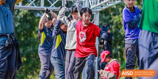 Students participate in a physical challenge by navigating a metal climbing structure during an outdoor team-building or sports activity at Beijing Chaoyang KaiWen Academy.
