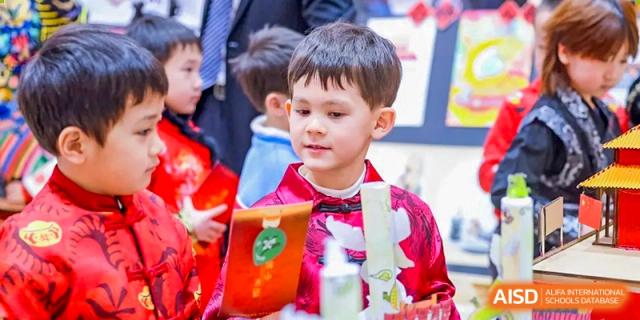 A young student in a bright red traditional Chinese garment focuses on a cultural activity during a festive celebration held on the campus of Beijing Chaoyang KaiWen Academy.