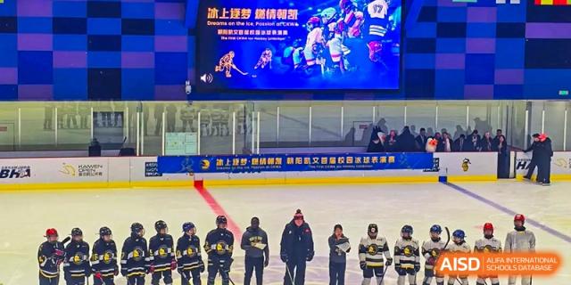 A youth ice hockey team in full gear stands in a line on the rink while a large digital screen displays game highlights at Beijing Chaoyang KaiWen Academy.