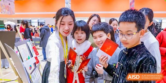 Students in red and white festive attire gather together to look at red envelopes and traditional decorations during a Lunar New Year event at Beijing Chaoyang KaiWen Academy.