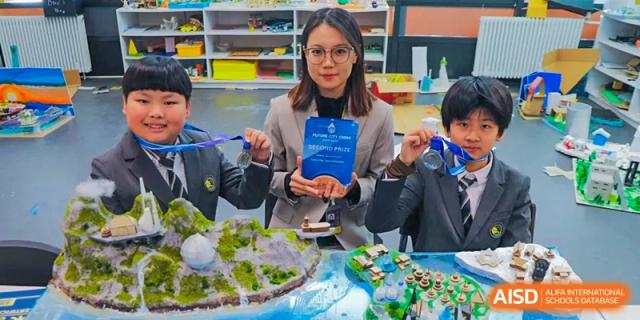 A teacher and two students proudly display an award plaque and medals for their achievement in a science or geography project at Beijing Chaoyang KaiWen Academy.