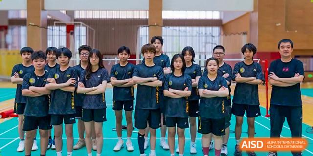 A group of male and female students in athletic wear stands with arms crossed on an indoor court while posing for a team portrait before a sports match at Beijing Chaoyang KaiWen Academy.