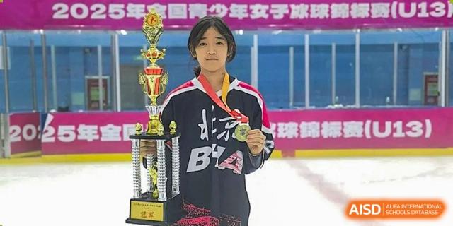A female student athlete proudly displays a gold medal and a large trophy while standing on the ice rink after a successful hockey tournament at Beijing Chaoyang KaiWen Academy.