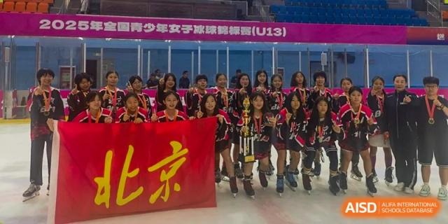 A female youth hockey team in red and black uniforms gathers on the ice behind a large red banner to celebrate their championship victory at Beijing Chaoyang KaiWen Academy.