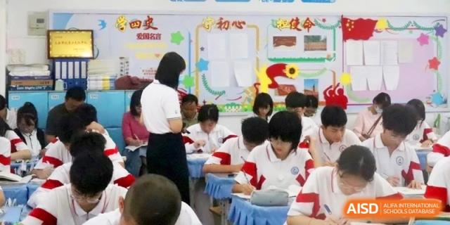Students in white and red uniforms focus on their lessons in a bright classroom while a teacher assists them at RDFZ Sanya School
