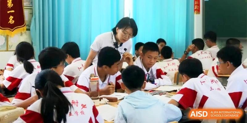 An educator leans over to provide personalized instruction to a group of students working together on a project in a bright classroom at RDFZ Sanya School