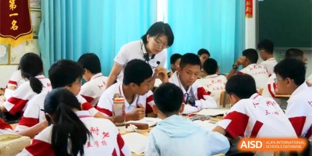 An educator leans over to provide personalized instruction to a group of students working together on a project in a bright classroom at RDFZ Sanya School