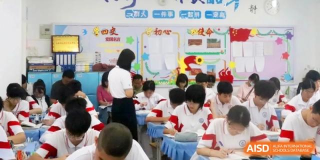 A teacher in a white polo shirt stands by a desk guiding students through their coursework during a focused classroom session at RDFZ Sanya School