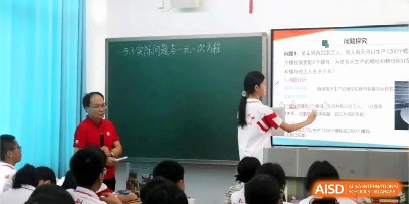 A student stands at the front of the classroom by a chalkboard and a digital display to present a lesson to her peers at RDFZ Sanya School