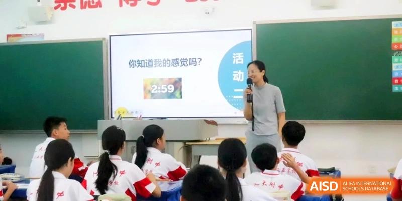 An educator smiles while addressing a class of students during a presentation using a digital screen with a countdown timer at RDFZ Sanya School