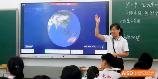 An instructor gestures toward a digital display showing a globe of the Earth while teaching a lesson to focused students at RDFZ Sanya School