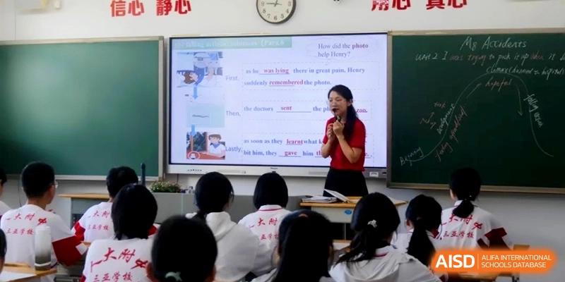 A teacher in a red shirt stands before a large digital screen with text and images to explain a lesson to the class at RDFZ Sanya School