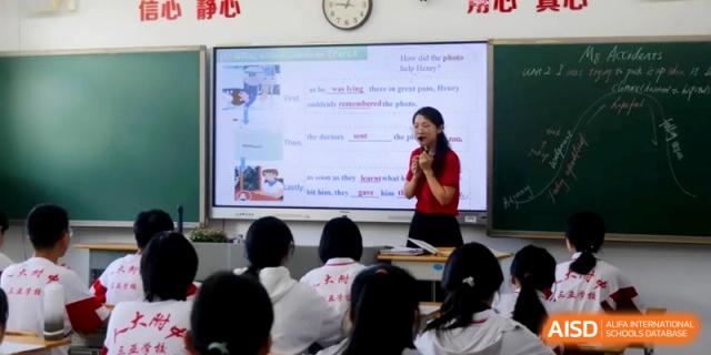 A teacher in a red shirt stands before a large digital screen with text and images to explain a lesson to the class at RDFZ Sanya School
