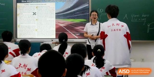 A teacher uses a microphone to lead a discussion while a digital screen shows a sports track image to a class of attentive students at RDFZ Sanya School