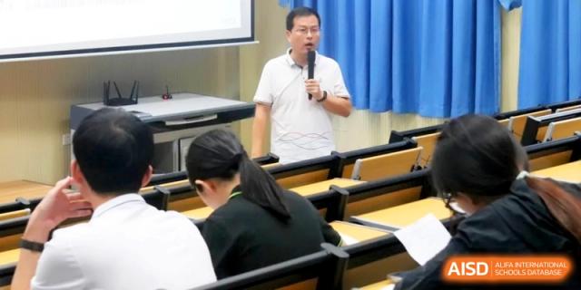 A male teacher in a white polo shirt leads a lecture in a large lecture hall while students take notes at their desks at RDFZ Sanya School