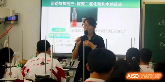 An educator explains a science experiment involving carbon dioxide and water while using a digital screen to guide the class at RDFZ Sanya School