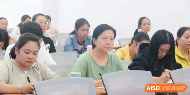 A woman in a green shirt sits at a desk and listens attentively during a classroom session or educational seminar at RDFZ Sanya School