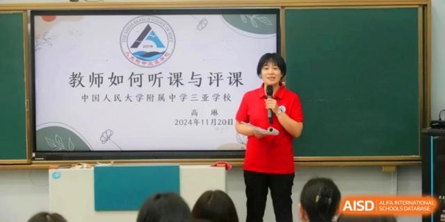 A teacher in a red shirt stands in front of a digital screen and chalkboard to deliver a presentation to an audience at RDFZ Sanya School