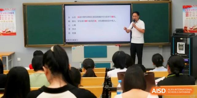 An instructor gestures toward a digital whiteboard with text while speaking into a microphone during an interactive classroom session at RDFZ Sanya School