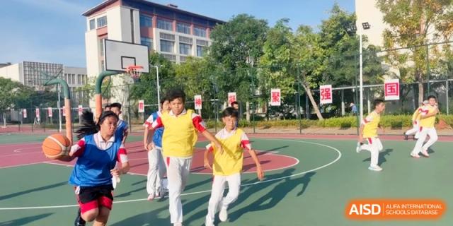 A group of students in activewear run across a bright green and red outdoor sports court during a physical education class at RDFZ Sanya School